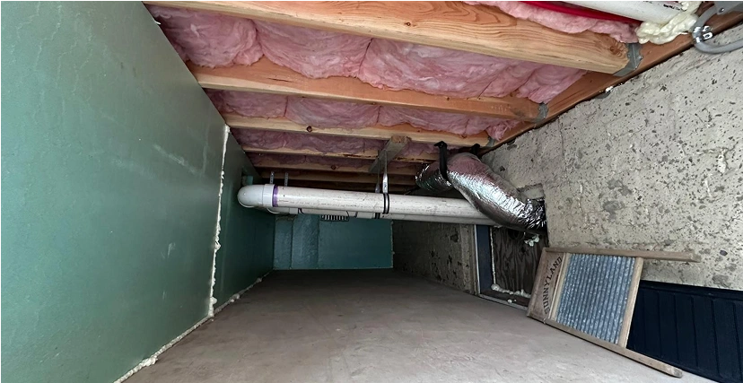 Crawl space with exposed insulation and pipes.