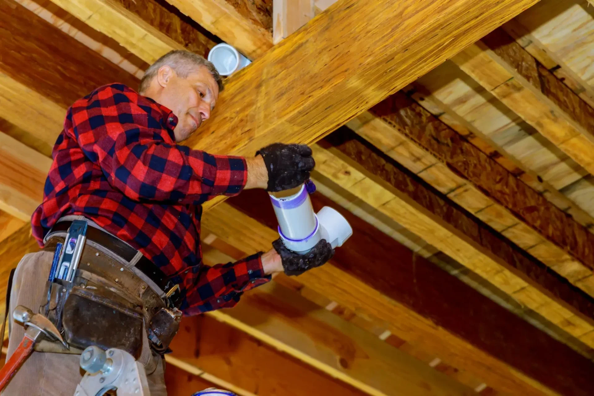 Man installing ductwork in wooden ceiling.